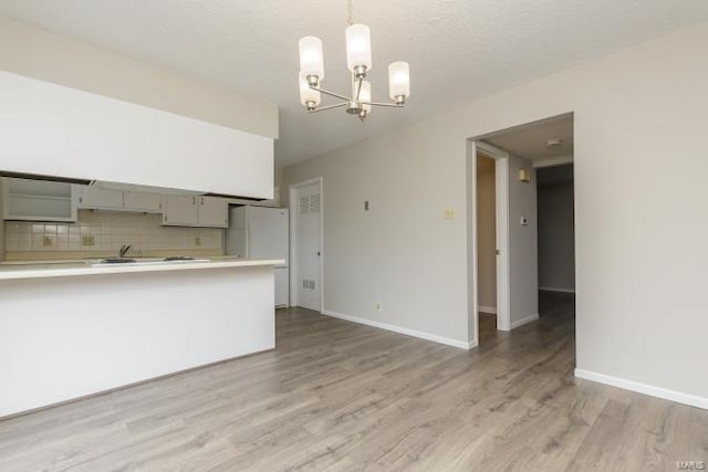 kitchen with a notable chandelier, light wood-style floors, decorative backsplash, light countertops, and decorative light fixtures