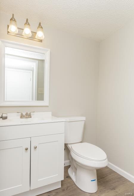 half bathroom featuring baseboards, toilet, vanity, and wood finished floors