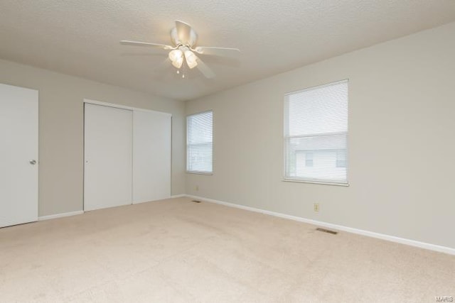 unfurnished bedroom with light carpet, visible vents, baseboards, a closet, and ceiling fan