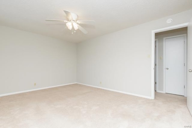 empty room with light colored carpet, ceiling fan, baseboards, and a textured ceiling
