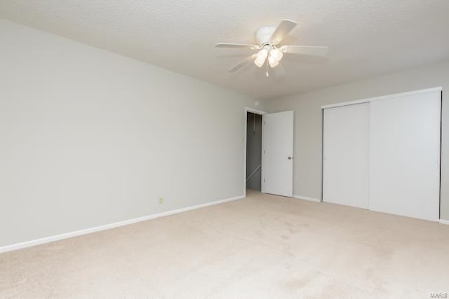 unfurnished bedroom featuring light carpet, baseboards, a textured ceiling, and a closet