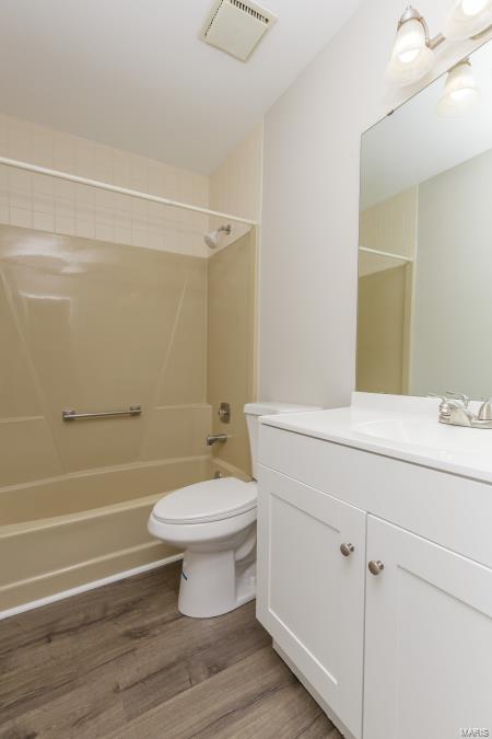 full bathroom with wood finished floors, shower / bathing tub combination, vanity, toilet, and visible vents