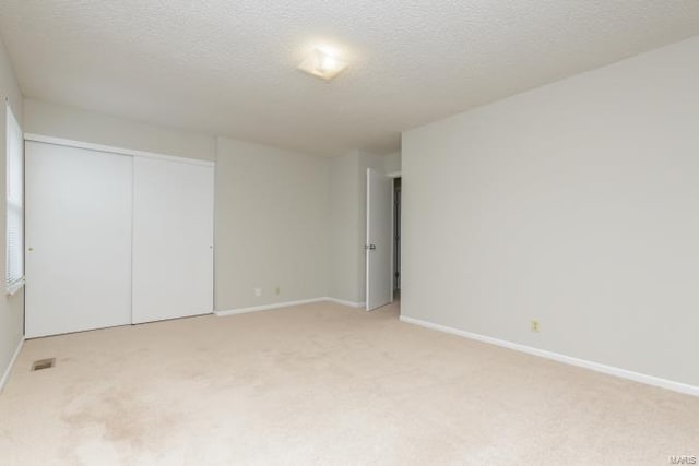unfurnished bedroom with light colored carpet, baseboards, and a textured ceiling