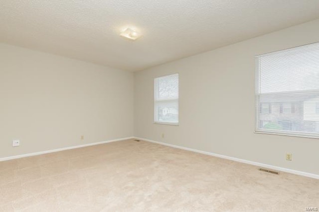 empty room featuring visible vents, light carpet, baseboards, and a textured ceiling