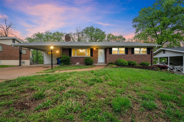 single story home with driveway, a chimney, a lawn, brick siding, and an attached carport