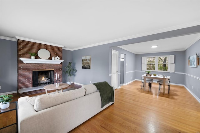 living room with a fireplace, baseboards, crown molding, and light wood-type flooring