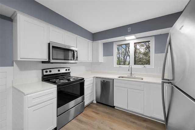 kitchen with appliances with stainless steel finishes, a sink, light countertops, light wood-style flooring, and white cabinetry