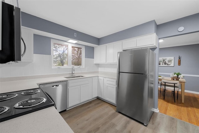 kitchen with white cabinets, appliances with stainless steel finishes, a sink, light countertops, and light wood-type flooring