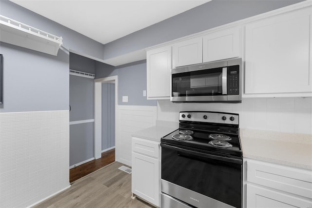 kitchen featuring appliances with stainless steel finishes, light countertops, light wood-style flooring, white cabinetry, and tasteful backsplash