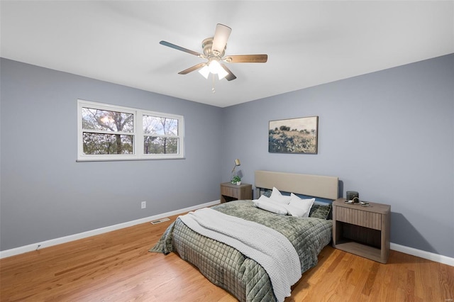 bedroom featuring baseboards, a ceiling fan, wood finished floors, and visible vents