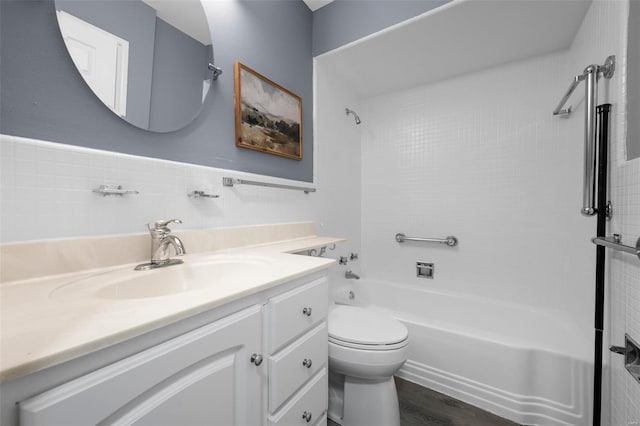 bathroom with vanity, bathtub / shower combination, toilet, a wainscoted wall, and tile walls