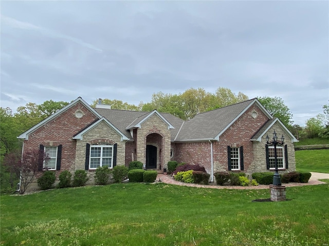 view of front facade with brick siding, a front yard, a shingled roof, and stone siding