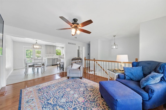 living area with visible vents, light wood finished floors, ceiling fan, and baseboards
