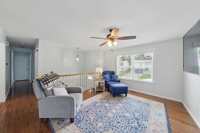 living area featuring a ceiling fan, baseboards, an upstairs landing, and wood finished floors
