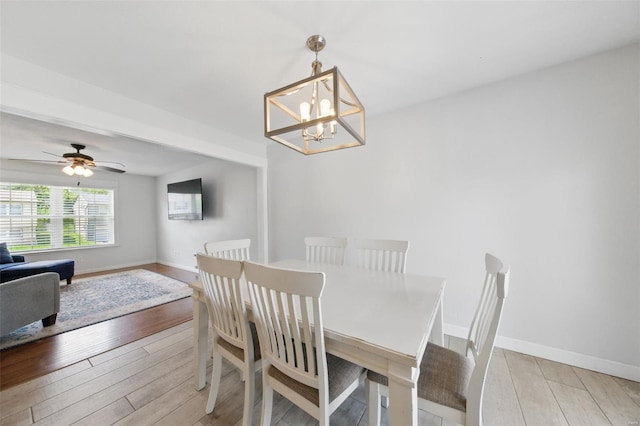 dining room with baseboards, light wood-style flooring, and ceiling fan with notable chandelier