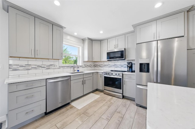 kitchen with tasteful backsplash, a sink, light wood-style flooring, gray cabinetry, and stainless steel appliances