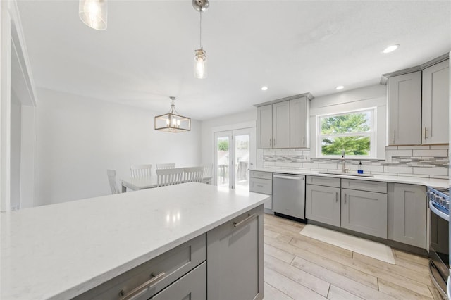 kitchen with a sink, gray cabinets, light wood-style flooring, stainless steel appliances, and backsplash