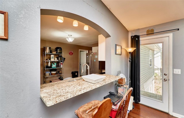 kitchen featuring arched walkways, stainless steel fridge with ice dispenser, wood finished floors, and a wealth of natural light