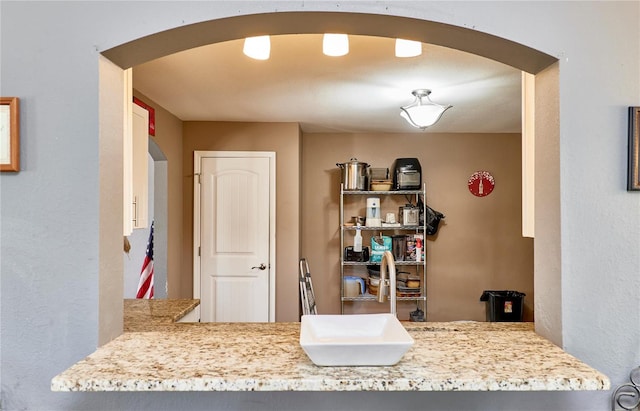 kitchen featuring arched walkways, a sink, and light stone counters