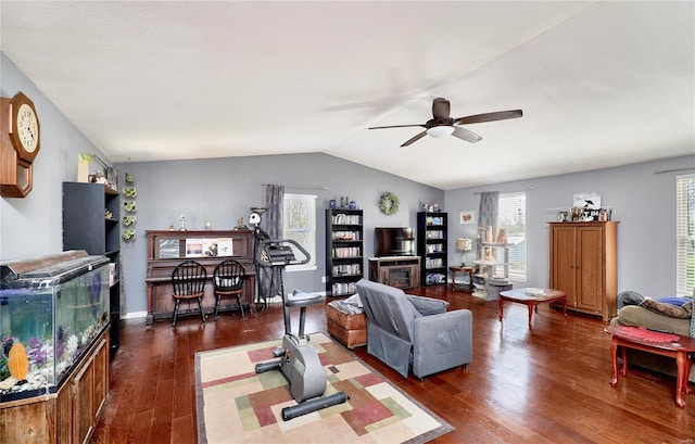 living area with dark wood-type flooring, vaulted ceiling, a fireplace, and a ceiling fan