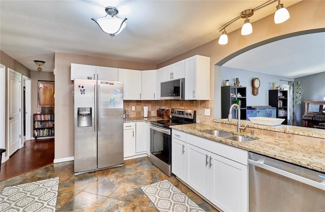 kitchen with tasteful backsplash, arched walkways, a sink, appliances with stainless steel finishes, and light stone counters
