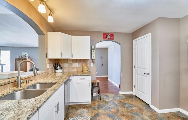 kitchen featuring baseboards, white cabinets, a sink, stone finish floor, and backsplash