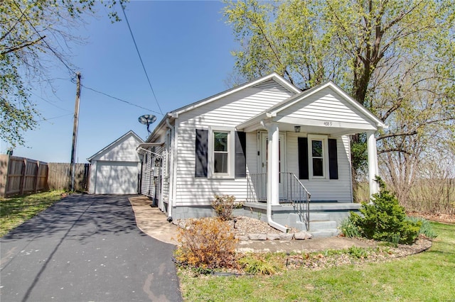 bungalow-style home featuring driveway, covered porch, fence, a garage, and an outdoor structure