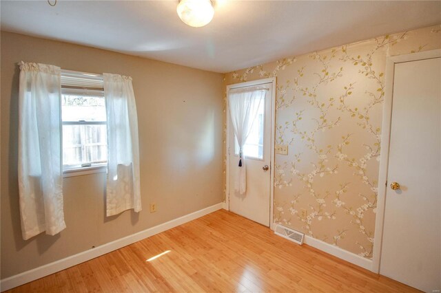 empty room with light wood-type flooring, visible vents, and baseboards