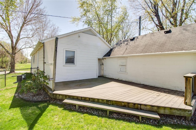 rear view of property featuring fence, a lawn, roof with shingles, and a deck