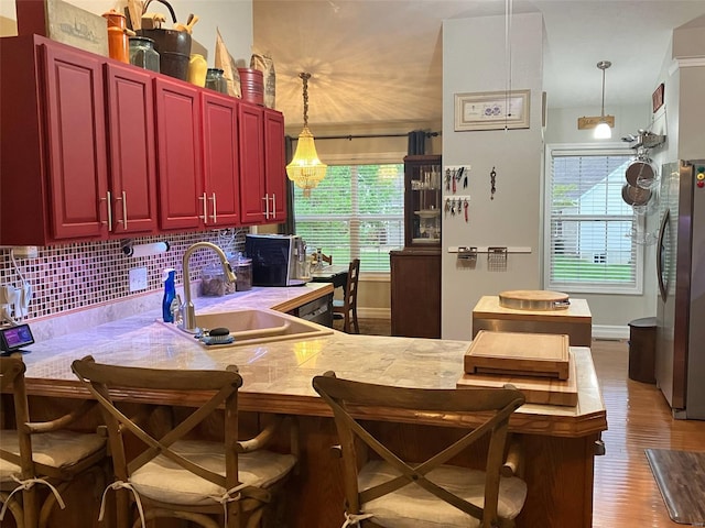 kitchen featuring freestanding refrigerator, wood finished floors, a healthy amount of sunlight, a sink, and backsplash