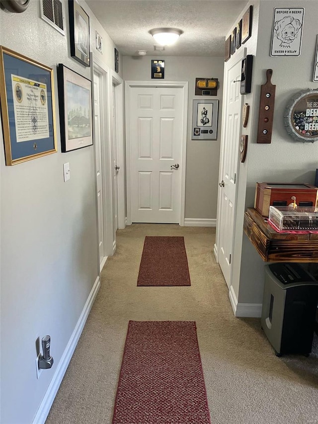 hallway featuring visible vents, a textured ceiling, baseboards, and light carpet