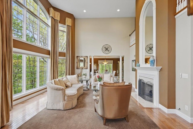 living area with a fireplace with flush hearth, plenty of natural light, wood finished floors, and a towering ceiling