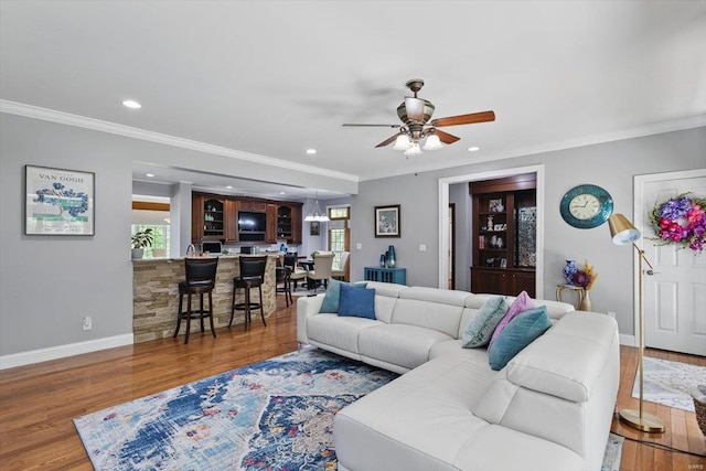living area with ceiling fan, ornamental molding, and wood finished floors