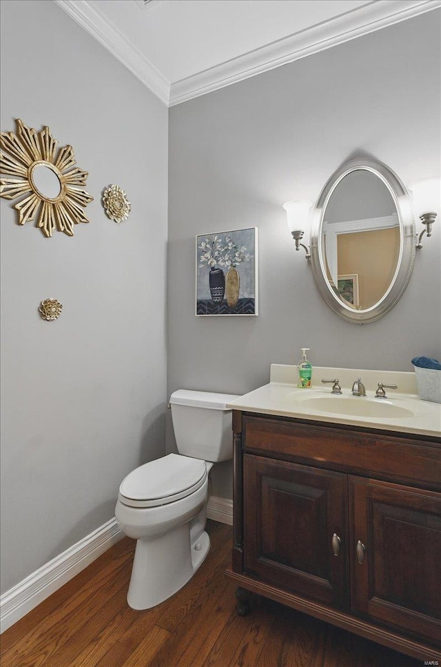 half bathroom featuring wood finished floors, baseboards, vanity, toilet, and ornamental molding
