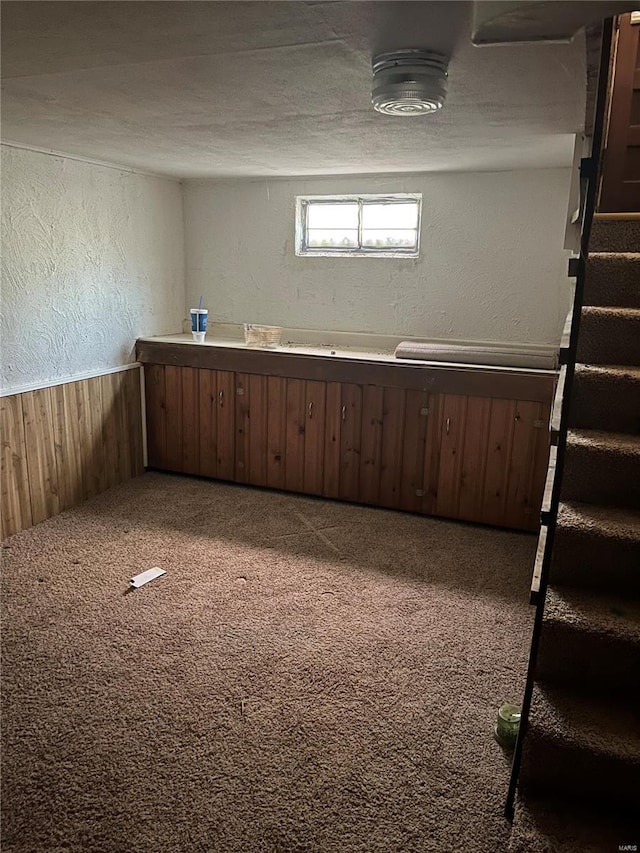 below grade area with a textured wall, wood walls, carpet floors, and stairway