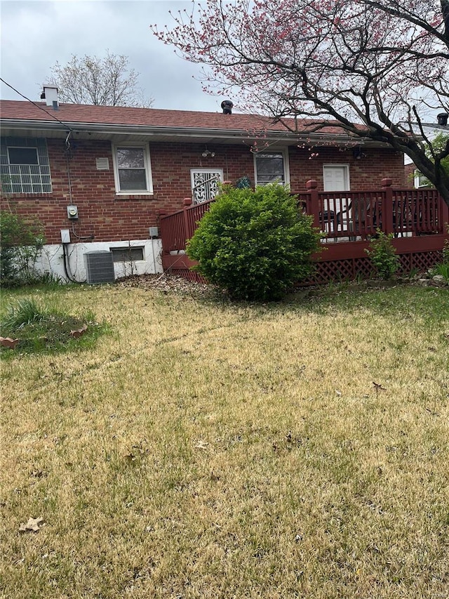 back of property with a lawn, central AC unit, brick siding, and a deck