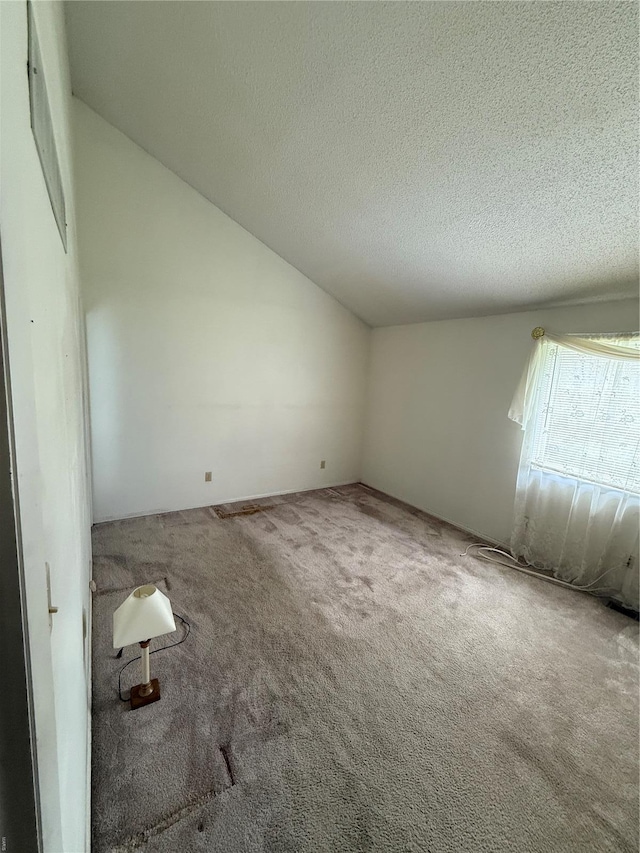 carpeted empty room featuring vaulted ceiling and a textured ceiling