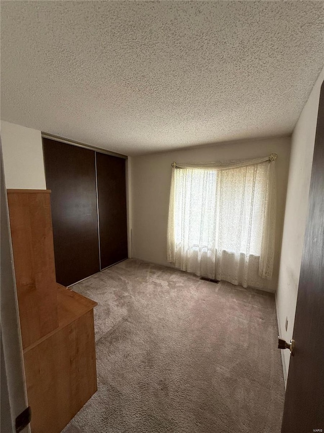 unfurnished bedroom with a closet, a textured ceiling, visible vents, and carpet