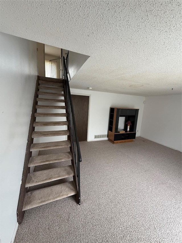 stairs with carpet flooring, a textured ceiling, and visible vents