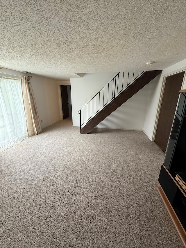 unfurnished living room featuring carpet flooring, stairs, and a textured ceiling