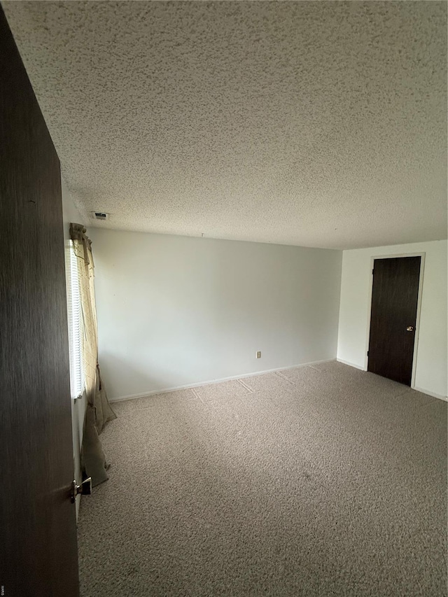 unfurnished room with a textured ceiling, carpet, and visible vents