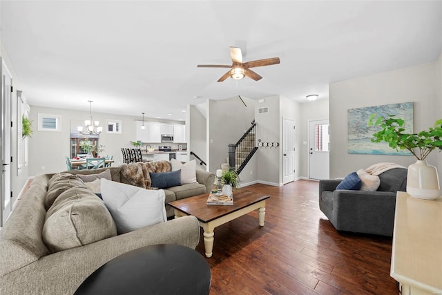 living room with plenty of natural light, dark wood-type flooring, stairway, and ceiling fan with notable chandelier