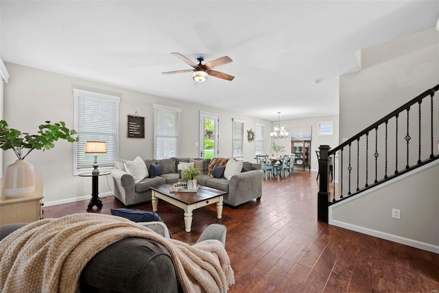 living room with dark wood-style flooring, stairway, baseboards, and ceiling fan with notable chandelier