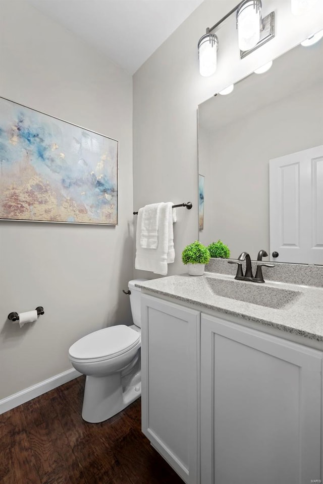 half bathroom featuring toilet, baseboards, wood finished floors, and vanity