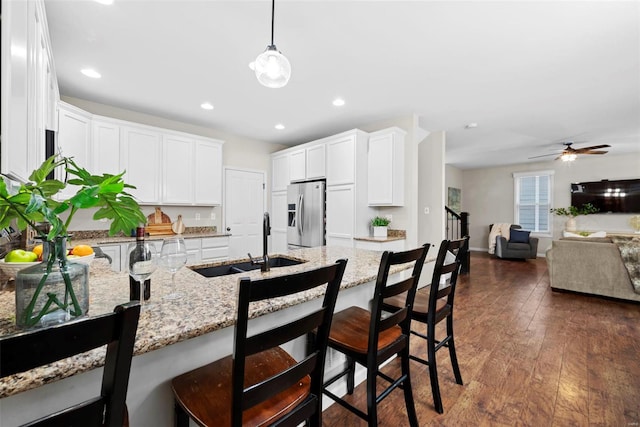 kitchen featuring a sink, stainless steel fridge with ice dispenser, a kitchen breakfast bar, and light stone countertops