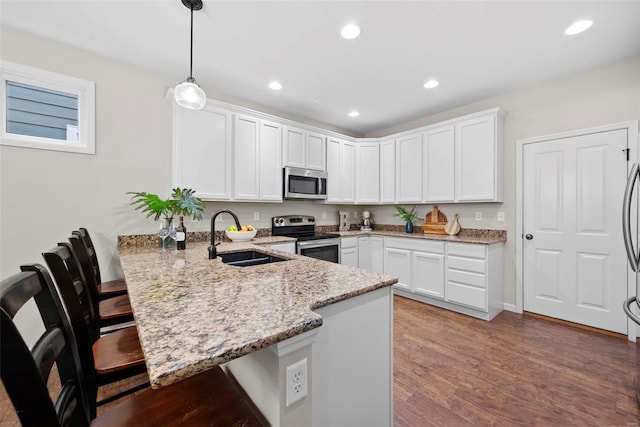 kitchen featuring a sink, stainless steel appliances, white cabinetry, a peninsula, and a kitchen bar
