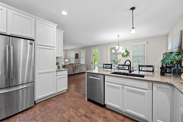 kitchen with white cabinets, appliances with stainless steel finishes, an inviting chandelier, a sink, and dark wood-style floors