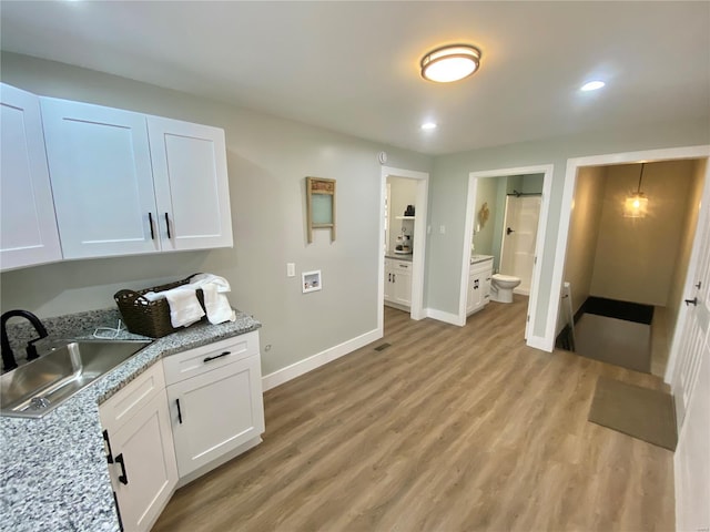 interior space with a sink, baseboards, light wood-style floors, white cabinetry, and light stone countertops