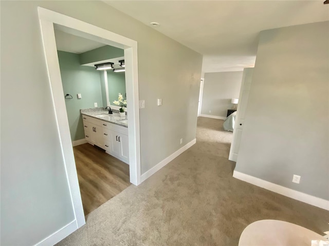 corridor with baseboards, light colored carpet, and a sink