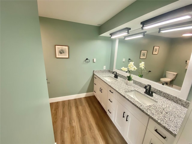 bathroom featuring wood finished floors, a sink, double vanity, and toilet